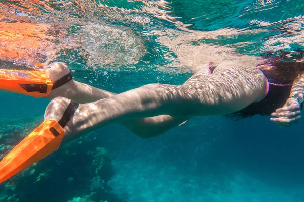 Mädchenbeine in orangefarbenen Schwimmflossen tauchen unter Wasser im Meer in der Nähe von Korallen — Stockfoto