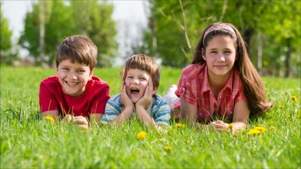 Drie kinderen liggen samen op groene weide — Stockvideo