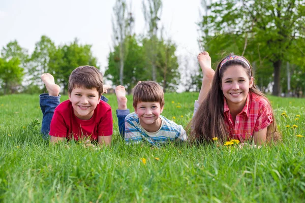 Drei lächelnde Kinder liegen zusammen auf der grünen Wiese — Stockfoto