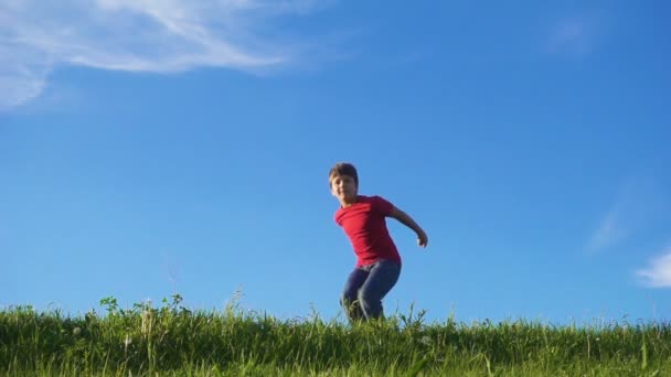 Niño feliz saltando en la colina verde hierba contra el cielo azul — Vídeo de stock