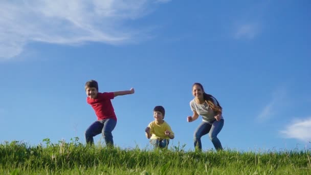 Familia feliz saltando en la colina hierba verde contra el cielo azul — Vídeos de Stock