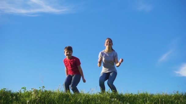 Niños felices saltando en la colina verde hierba contra el cielo azul — Vídeos de Stock