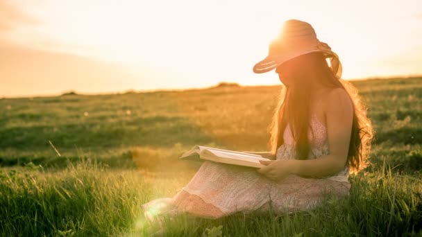 Chica leyendo el libro sobre el paisaje rural contra la puesta del sol — Vídeo de stock