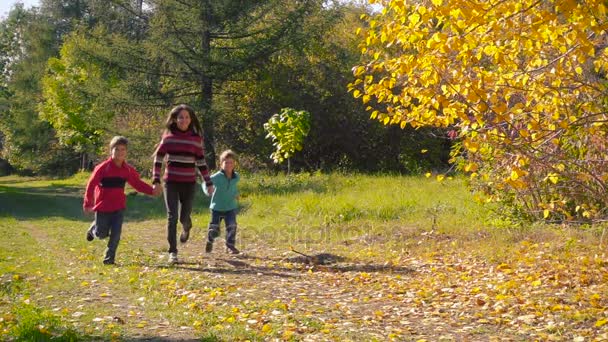 Троє щасливих дітей біжать разом в осінньому лісі — стокове відео