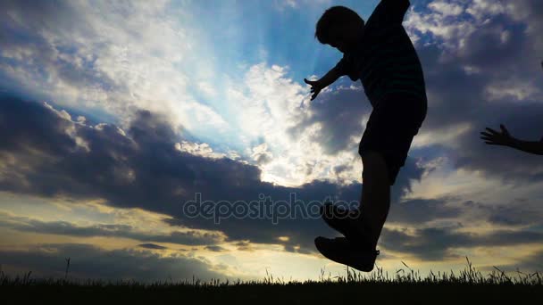 Silhouette of two boys jumping on field against sunset — Stock Video