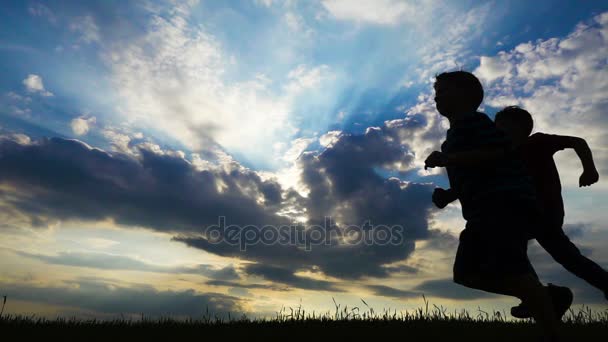 Silhouette von zwei Jungen, die gegen Sonnenuntergang auf ein Feld rennen — Stockvideo