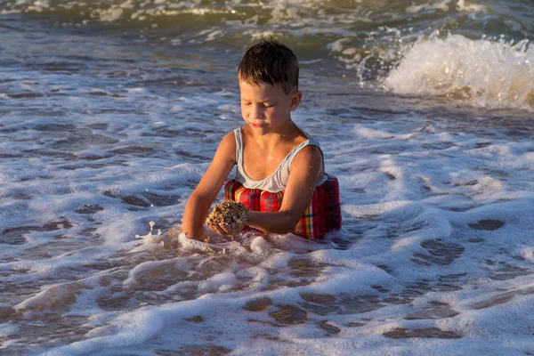 Petit garçon jouant avec le sable dans le surf de mer — Photo