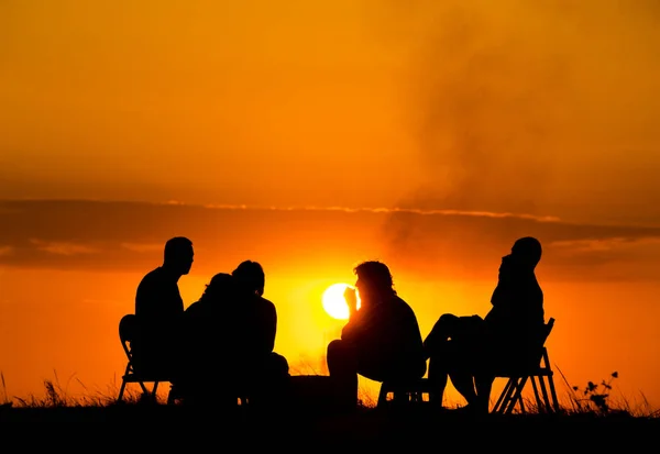 一群人在附近反对日落篝火野营坐 — 图库照片