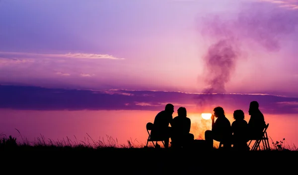 Personnes assises près du feu de camp contre le coucher du soleil avec copyspace — Photo