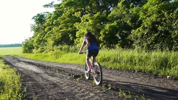 Chica joven montando en bicicleta en el camino del campo al atardecer — Vídeo de stock