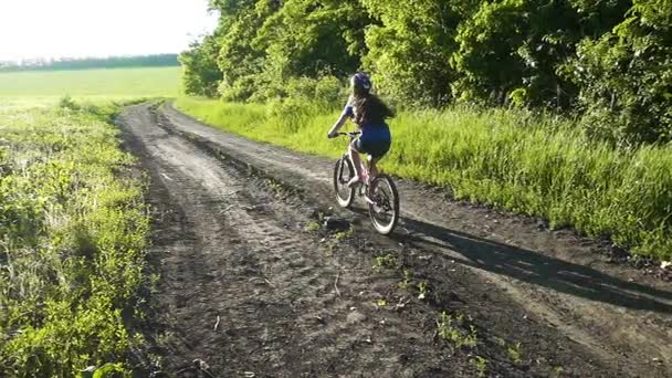 Mladá dívka na koni na kole na venkovské silnici při západu slunce — Stock video