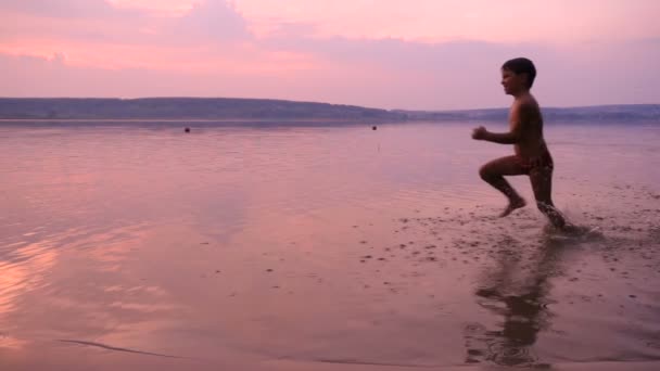 Zwei Jungen laufen zusammen am Strand des Flusses bei Sonnenuntergang — Stockvideo