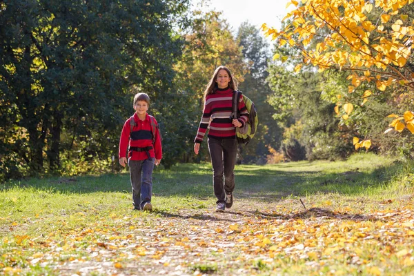 Duas crianças sorridentes no parque de outono com mochilas — Fotografia de Stock