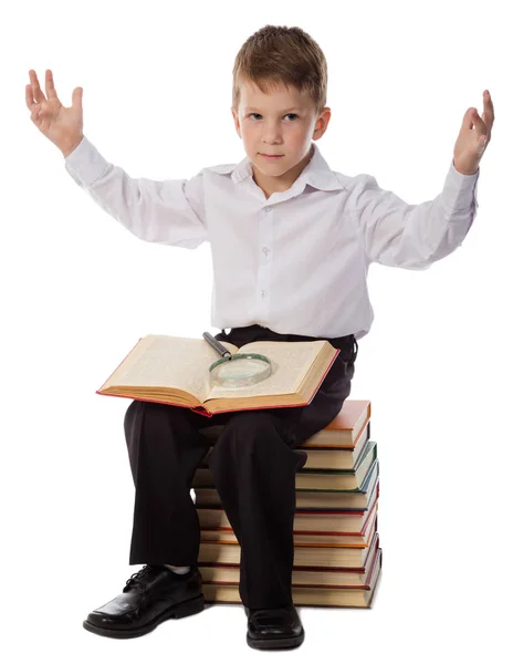 Surprised boy sitting on pile of books with magnifyer — Stock Photo, Image