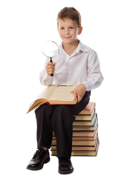 Smiling boy sitting on pile of old books with magnifier — Stock Photo, Image