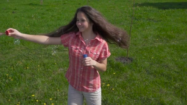 Jovem menina girar com bolhas de sabão no parque de primavera — Vídeo de Stock