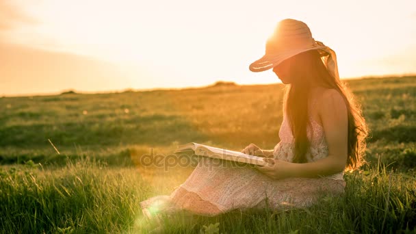 Menina lendo o livro sobre paisagem rural ao pôr do sol — Vídeo de Stock