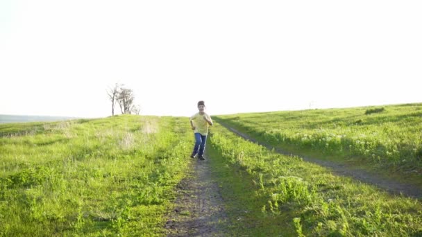 Мальчик бежит по сельской дороге на зеленом травяном поле — стоковое видео