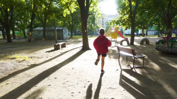 Chlapec běží na dvoře za deště se slunečním — Stock video