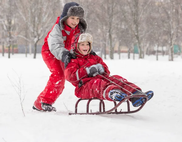 Два счастливых мальчика катаются на горке по снежному городскому парку — стоковое фото