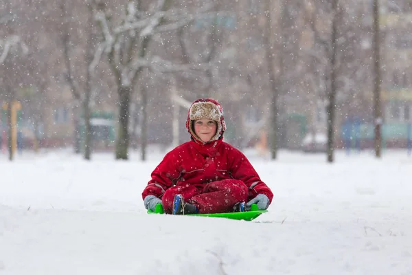 Lachende jongen zitten bij dia op besneeuwde landschap — Stockfoto