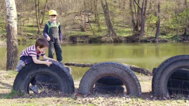 Dos niños jugando juntos saltando y subiendo sobre neumáticos viejos — Vídeo de stock