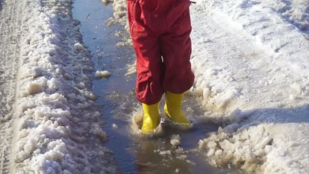 Niño en botas de lluvia saltando en el charco de hielo — Vídeos de Stock