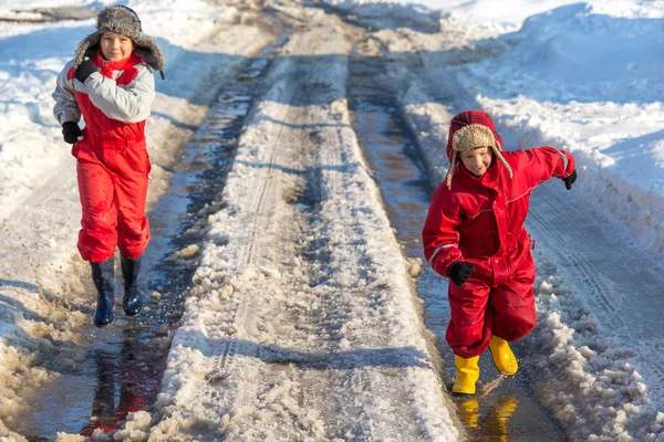 Двое детей в дождевых сапогах бегают по луже льда — стоковое фото