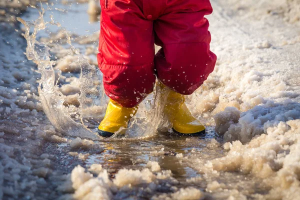 Парень в дождевых сапогах прыгает в лужу со льдом — стоковое фото