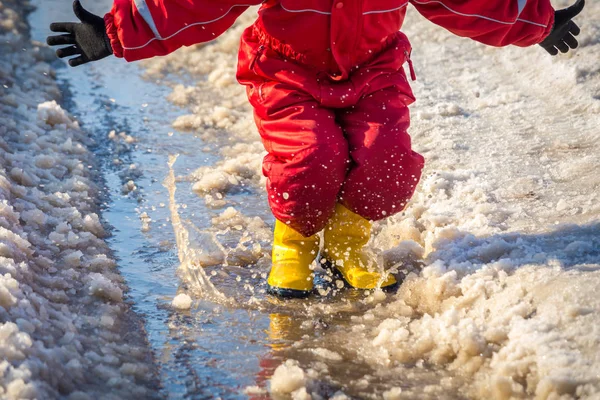 Kid in regenlaarsjes springen in de plas van ijs — Stockfoto