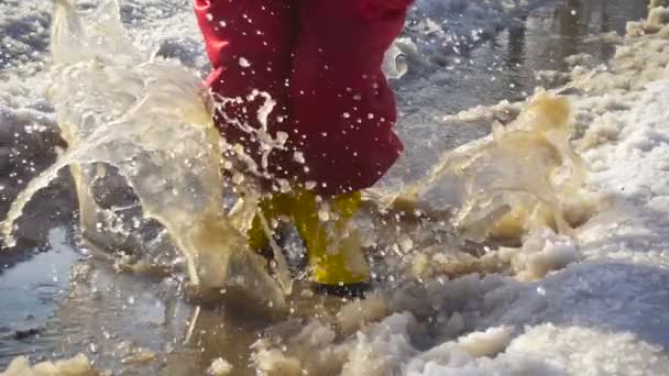 Дитина в дощових чоботях стрибає в льоду калюжі — стокове відео