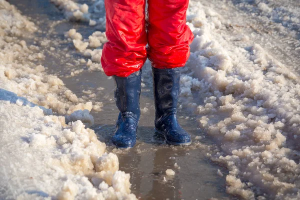 Kid benen in regenlaarsjes staande in de plas van ijs — Stockfoto