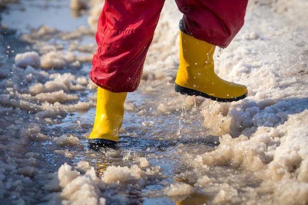 Pernas de criança em botas de chuva correndo na poça de gelo — Fotografia de Stock