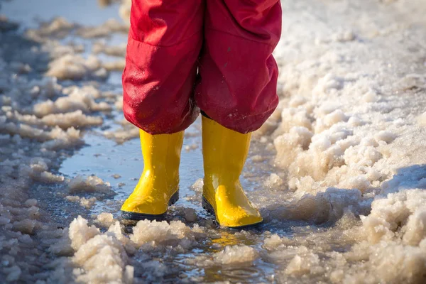 Kid benen in regenlaarsjes staande in de plas van ijs — Stockfoto