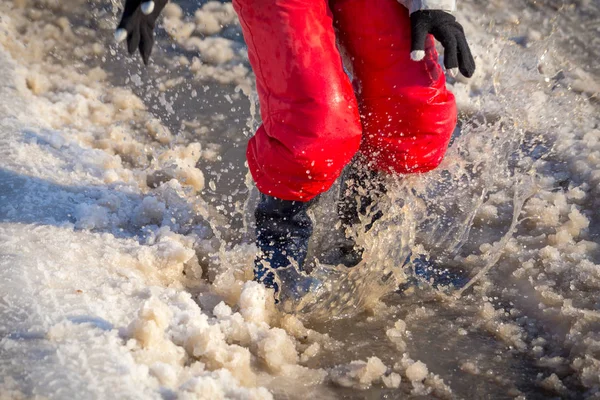Kid in regenlaarsjes springen in de plas van ijs — Stockfoto