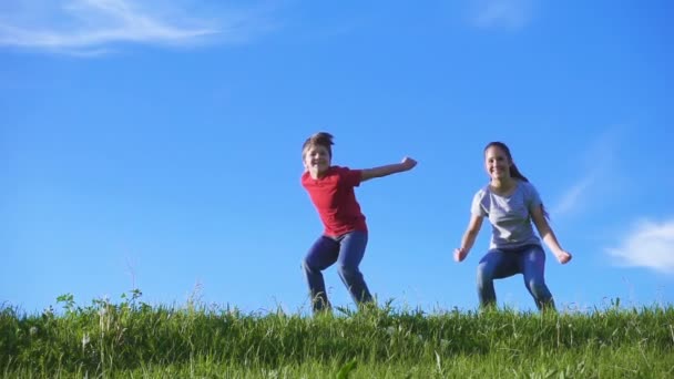 Glückliche Kinder springen gemeinsam auf grünem Grashügel vor blauem Himmel — Stockvideo