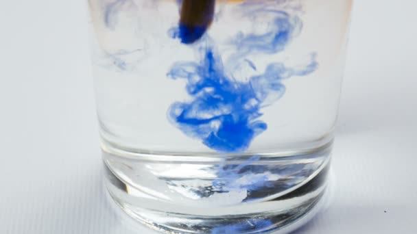 Blauwe aquarel verf druppels ontbinden op water in glas — Stockvideo