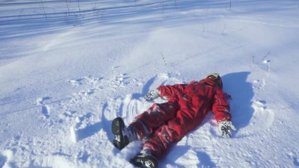 Happy kid on winter park making snow angel — Stock Video