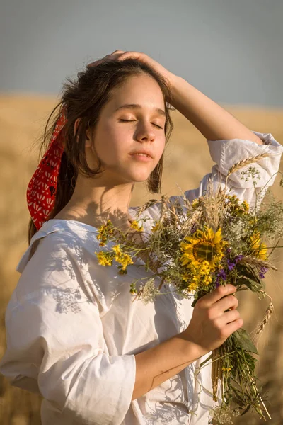 Girl on straw field with wildflower bouquet on hand — Stock Photo, Image