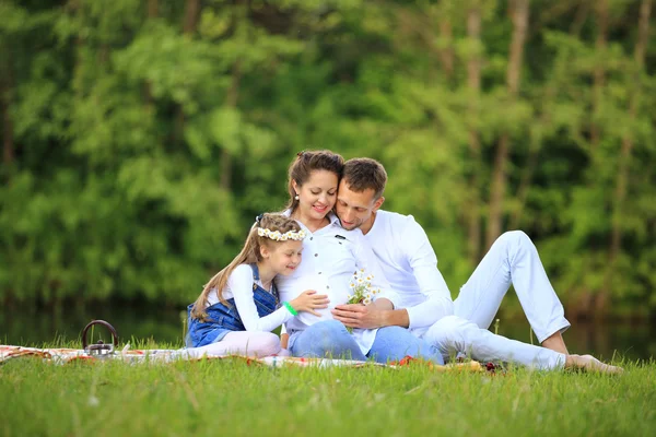 Feliz padre de una hija y una madre embarazada en un picnic . — Foto de Stock