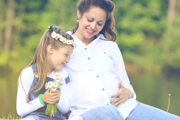 Embarazada mamá y su linda hijita en una corona de margaritas —  Fotos de Stock