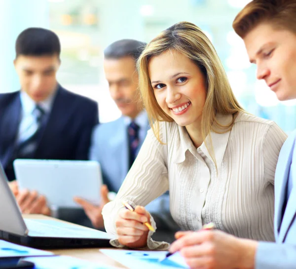 Smiling businesswoman posing while colleagues talking together in bright office — Stock Photo, Image