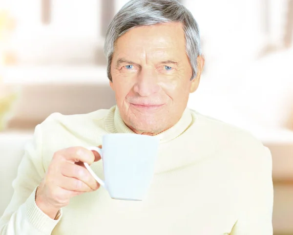 Retrato del hombre mayor sosteniendo taza de café, sonriendo a la cámara — Foto de Stock