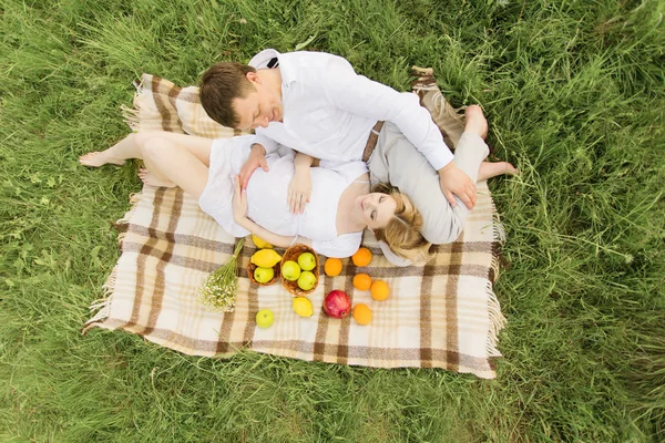 Ευτυχισμένο ζευγάρι - έγκυος γυναίκα και ο σύζυγός της κείνται σε μια κουβέρτα πικ-νικ στο γρασίδι — Φωτογραφία Αρχείου