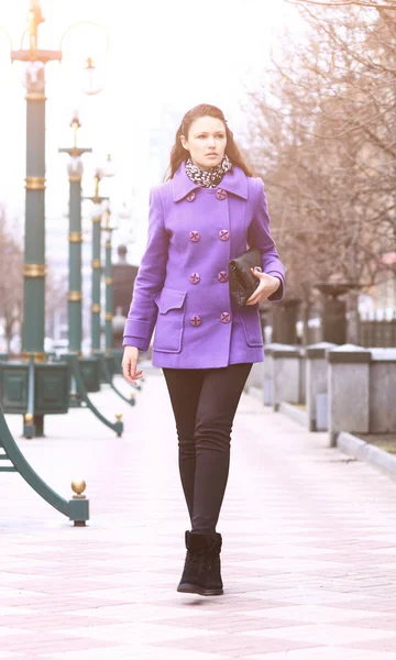 Beautiful girl walking down the street in a purple coat in clear time of day — Stock Photo, Image