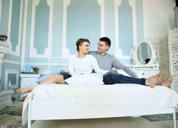 Junges glückliches Paar sitzt im Bett in geräumigem Schlafzimmer — Stockfoto