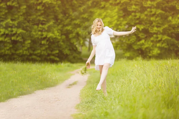 Pregnant woman walking in the park barefoot walking on carpet, holding shoes in hands — Stock Photo, Image