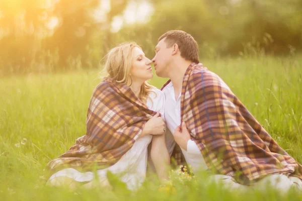 Pareja feliz - mujer embarazada y su marido cubierto con una manta sentarse en la hierba en el Parque —  Fotos de Stock