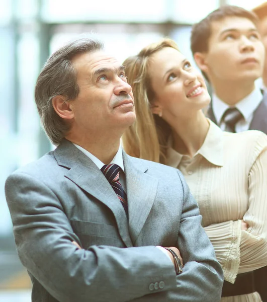 Bonne équipe d'affaires souriante debout dans une rangée dans le bureau et regardant vers le haut de la publicité virtuelle — Photo