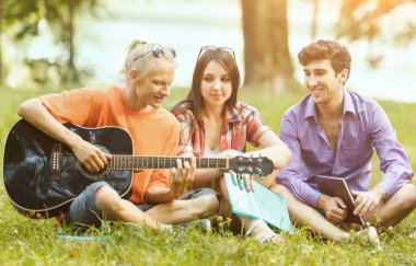 Güneşli bir günde parkta oturan bir gitar ile öğrenci grubu